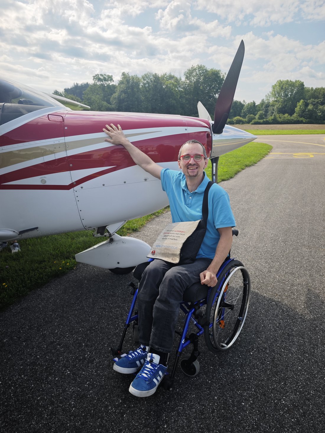 Erwin Strobl im Rollstuhl neben einem kleinen Flugzeug, der Arm ist zum Gruß erhoben