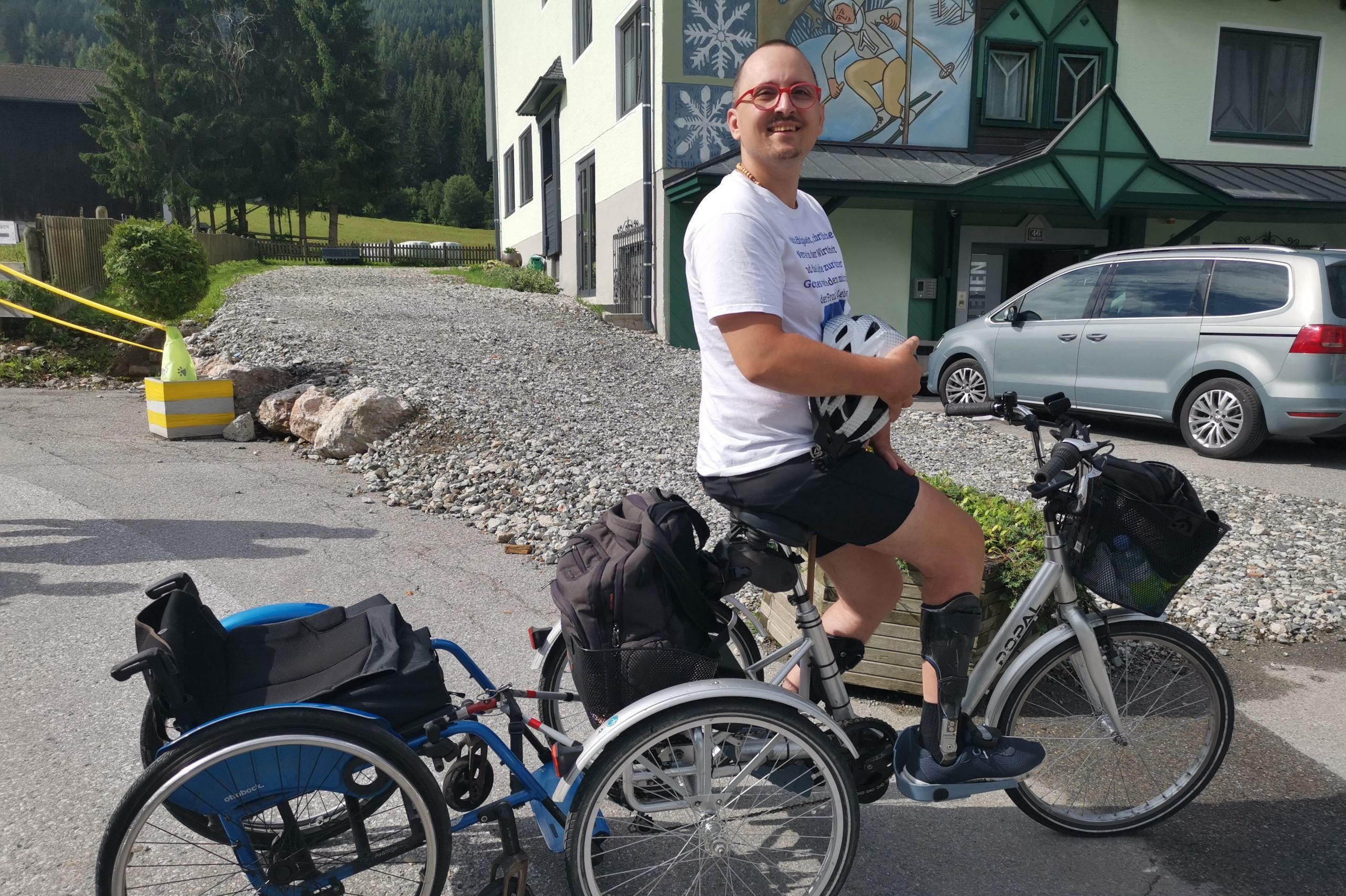 Erwin sitzt auf seinem Dreirad mit Rollstuhl hinten angehängt in Radstadt.